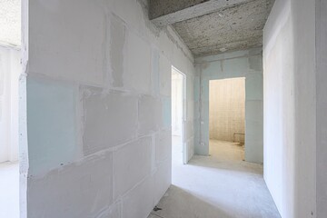 bright, unfinished interior shows walls covered in plasterboard, concrete ceilings, and empty doorways leading to other rooms