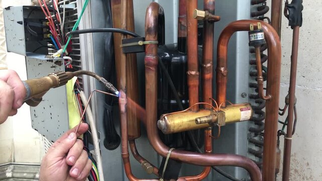 HVAC System Repair: A technician meticulously uses a torch to solder a copper pipe within an air conditioning system, highlighting precision and expertise in this crucial maintenance task.