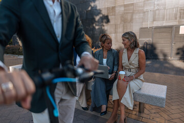 Businessman passing by businesswomen sitting and talking on a bench