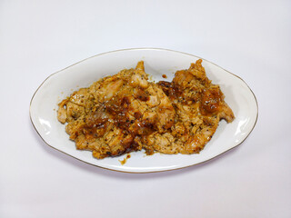 Chicken teriyaki, coated in a rich dark sauce with visible specks of black pepper, shows signs of being grilled and rests on a white plate against a blurred white background. Represents savory chicken
