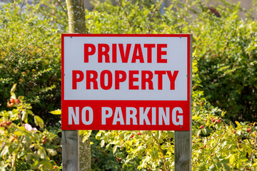 Sign that says "Private Property" and "No Parking" is posted in a green area