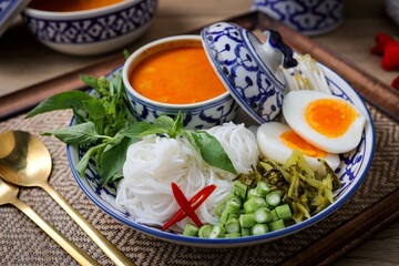Kanomjeen namya krati ,Rice vermicelli with minced fishes and coconut milk in red curry on ceramic plate side dish with vegetables and boiled egg