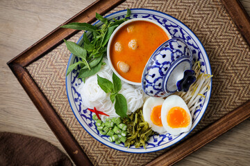 Kanomjeen namya krati ,Rice vermicelli with minced fishes and coconut milk in red curry on ceramic plate side dish with vegetables and boiled egg	