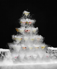 Ethereal mist envelops a whimsical tower of cocktail glasses, conjuring Gatsby-era glamour, perfect for Halloween or a steampunk celebration
