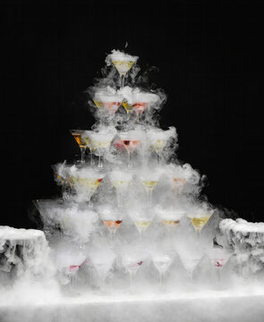 Ethereal mist envelops a whimsical tower of cocktail glasses, conjuring Gatsby-era glamour, perfect for Halloween or a steampunk celebration