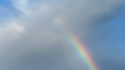 Translucent rainbow arc peeking through stormy clouds, evoking Celtic Imbolc feasts and unpredictable atmospheric wanderlust