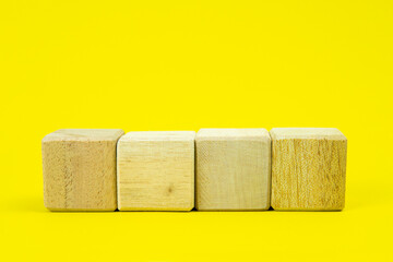 Four blank wooden blocks in a row on a yellow background with blank space for your text, letters or numbers.