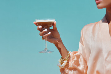 Woman holding espresso martini cocktail in elegant coupe glass on turquoise background