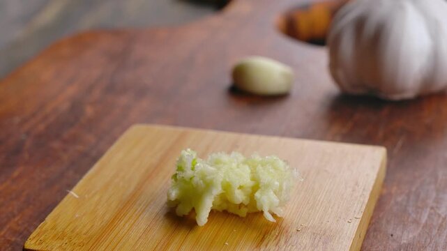 Close-up top view of a knife scraping freshly crushed garlic from a garlic press. Cooking preparation moment captured in a clean kitchen setting