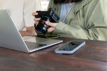 Woman checks photos on her digital camera with a laptop by her side, working or editing images.