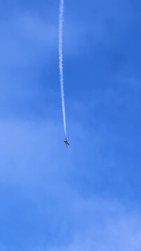 Jet descends vertically with contrail visible behind, highlighting dynamic nature of stunt flying in open sky environment with scattered clouds below. High level of pilot skill is required to sustain