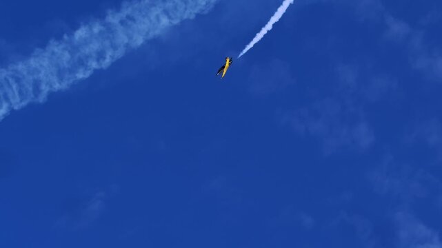 Fast-moving aircraft dives sharply against backdrop of deep blue sky and scattered clouds, with trail emphasizing direction and speed of maneuver. This vertical dive is part of planned aerobatic