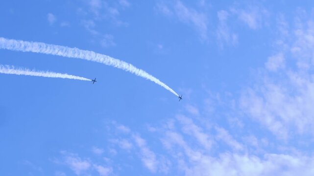 Group of five aircrafts flies closely together in synchronized flight, emitting white smoke trails that contrast vividly with light blue sky and scattered clouds above horizon.