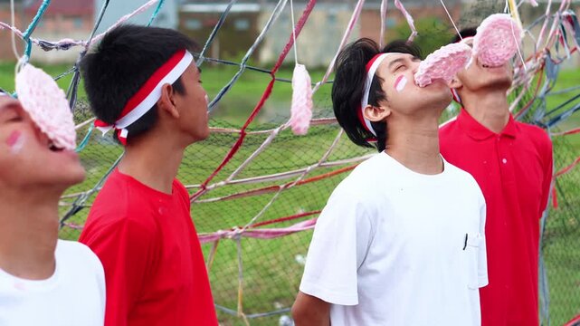 Group Of Young Indonesian Men With Headbands Intensely Participate In Traditional Cracker Eating Race