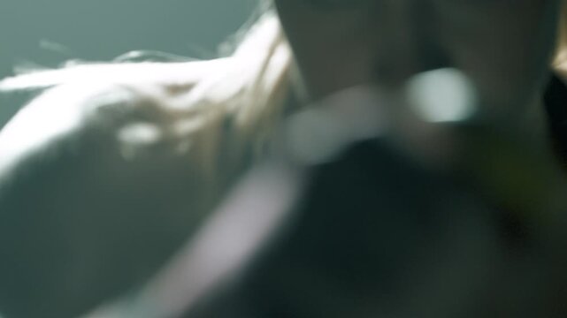 Close-up of blonde fit woman punching in the air with small yellow dumbbells. Her focused hands dominate the frame, occasionally revealing her intense eyes. Moody cinematic gym lighting