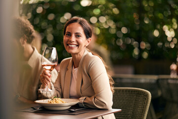 Smiling Woman Enjoying Wine and Dining Outdoors in a Relaxed Setting