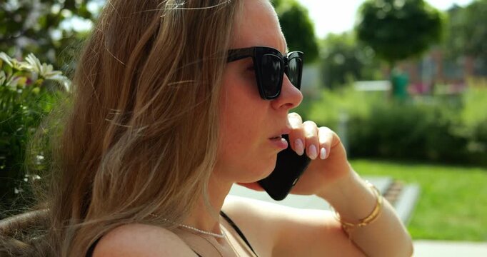 Woman holds phone to ear listening intently with lips slightly parted suggesting worry. Female focuses on serious phone conversation on sunny day in city park
