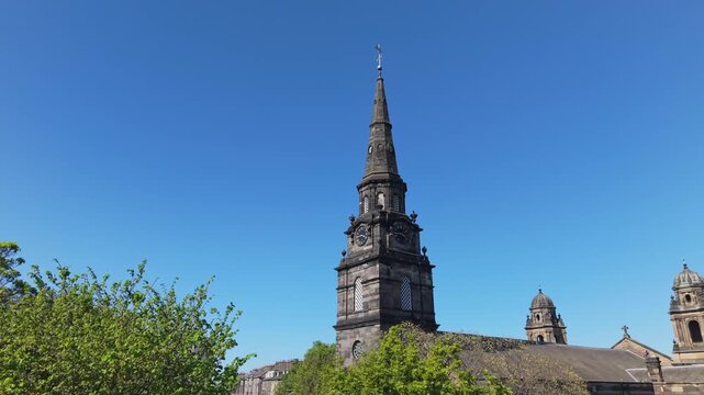 Drone footage revealing Edinburgh city on a bright morning, focusing on the parish church of St Cuthbert&rsquo;s tower, with clear skies and vibrant urban scenery