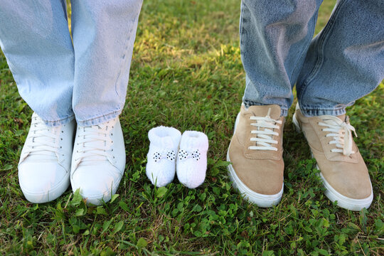 Two pairs of adult shoes standing on grass beside tiny white baby booties, beautifully symbolizing a growing family and the excitement of expecting a new member.