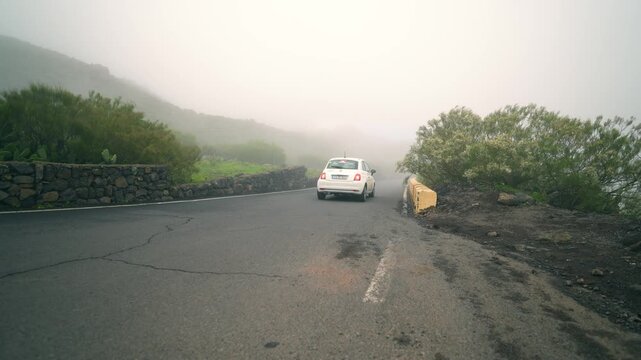 Foggy mountain road leading to Masca village with cars driving, filmed smoothly from low angle with stabilizer