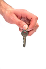 A hand grips a silver key with a distinct round hole at the top. The focus is on the metallic surface and intricate teeth of the key, set against a plain white backdrop