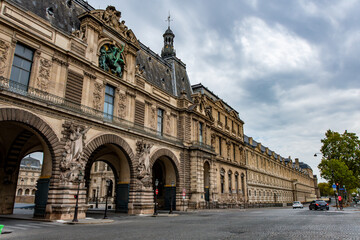 Stunning perspective of the Louvre Museum's historic architecture and the street life below under a cloudy sky.