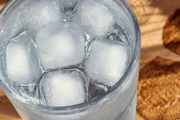 Ice cubes in a glass of water on a woven mat. Close-up of a clear glass filled with several large ice cubes and water. Selective focus.