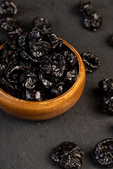 old wooden bowl filled with dried prunes made from plums, dark-colored dried plum fruits poured into a bowl
