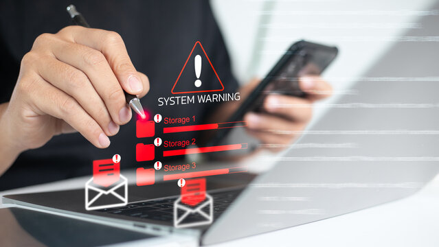 Close-up of a person checking a system warning on laptop showing storage overload, red alert icons, and email notifications. Concept of data management, IT system error, and digital risk warning.