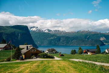 Cozy Scandinavian Homes Nestled in Verdant Valley with Majestic Mountain Views Overlooking Serene Blue Fjord on a Sunny Day