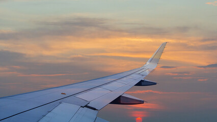 View from inside airplane flying above over sky in sunset light.