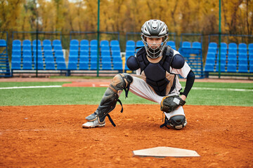 A good looking teenage boy squats in position on the baseball field, ready for action
