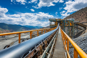Obraz premium Conveyor belt transports materials at a vibrant gold mine under a bright blue sky with fluffy clouds
