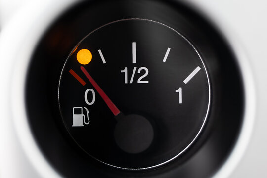 Car fuel gauge with pump pictogram, showing low fuel and waning orange light. Macro close up shot, no people