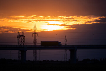 Truck with trailer crossing a bridge set against the setting sun. Backlight silhouette, telephoto shot