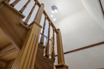 low-angle shot showcases a wooden staircase with ornate railings. Above, a modern chandelier hangs from a textured white ceiling, complementing the room's subtle wallpaper