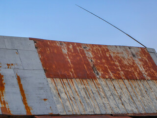 An aged metal roof exhibits a rusty and weathered appearance against a clear blue sky.