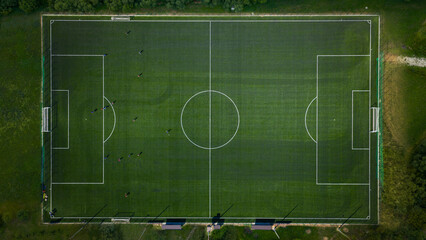 Aerial top-down shot of a green football field with visible players and clean white markings under daylight