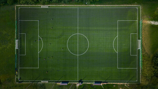 Aerial top-down shot of a green football field with visible players and clean white markings under daylight