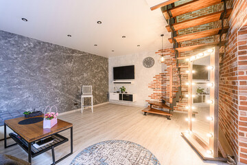 Modern living room with brick accent walls, spiral staircase, large mirror with lights, and stylish furniture