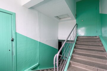 Stairwell with green doors, white and green walls, and concrete stairs with a metal railing