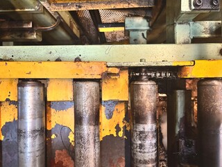 A close-up view of heavily used, dirty industrial machinery with peeling yellow paint and corroded metal rollers. The visible chain and sprocket, along with the grime, suggest a demanding factory or w