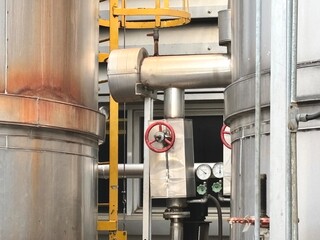 A close-up view of an intricate network of industrial pipes, valves with red handwheels, and large...