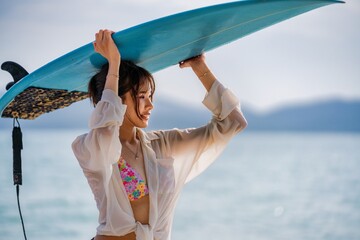 Woman enjoying a sunny day at the beach holding a surfboard over her head near the ocean