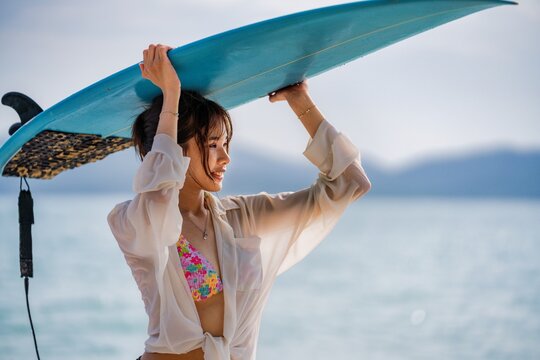 Woman enjoying a sunny day at the beach holding a surfboard over her head near the ocean
