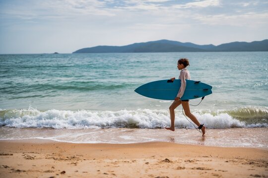 Surfer carrying a blue board walks along the sandy beach during a sunny day by the ocean