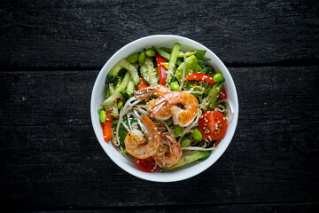 bibimbap with sprouts, shrimp, tomatoes, peppers, cucumbers and beans in a white plate on a dark background