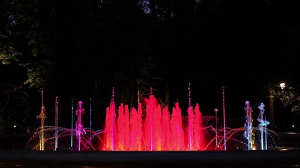 Illuminated fountain at night with colorful jets spraying high in the air. Vibrant light display against dark background creates magical atmosphere in city park. - Powered by Adobe