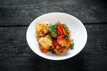 Korean chicken on a plate with sauce with pepper and herbs on a dark background