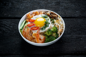 bowl with sprouts, shrimp, peppers, mushrooms and broccoli in a white plate on a dark background